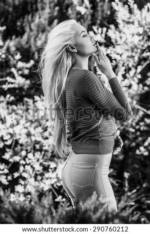 Outdoors portrait of beautiful & positive young blond girl in sweater. Person against nature. Black-white photo.