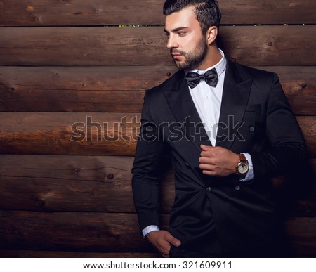 Portrait of young beautiful fashionable man against wooden wall In black suit & bow tie.