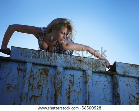 Elegant lady in an cocktail dress against old rusty container. Vogue style photo.