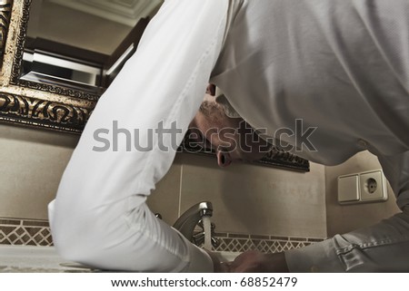 Man washing face in bathroom sink