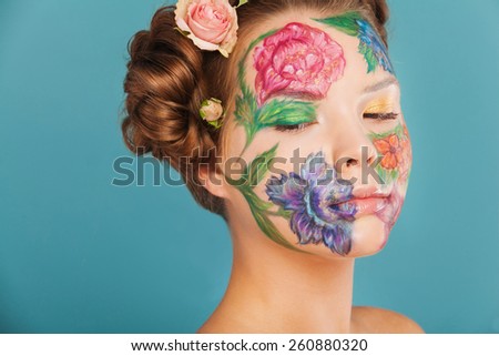 Spring portrait of model with hand drawing flowers on her face. Color face art woman. On blue background