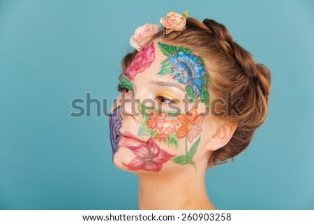 Woman model with hand drawing flowers on her face. Color face art woman. On blue background