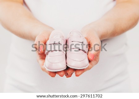 Pregnant woman holding pair of pink shoes for baby girl. Maternity and new family concept