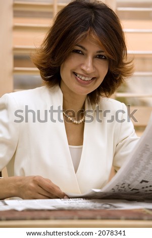 brunette smiling and holding newspaper wearing white suite