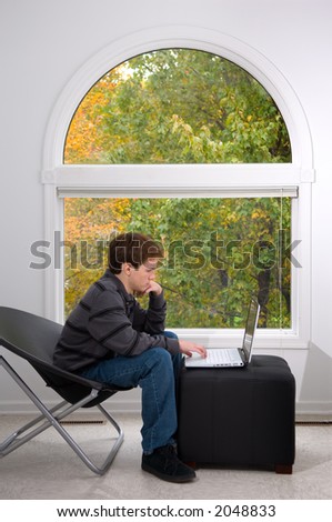 Teen male working with a notebook computer with fall foliage visible through a large window