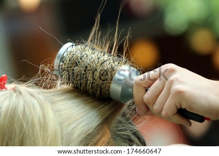 Hairdresser combing hair of young girl by hairbrush and hair dryer