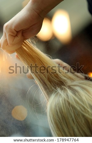 Hairdresser combing hair of young girl by hairbrush and hair dryer