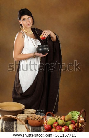 Young Roman woman with bowl and basket full of fruits and vegetables. Concept studio portrait on brown background.