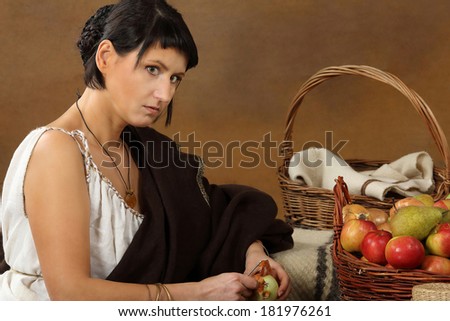 Young Romana peeling the onion with basket full of fruits and vegetables. Concept studio portrait on brown background.