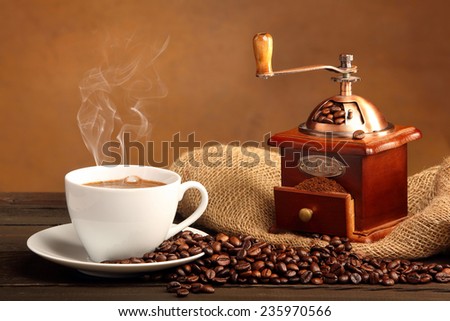 Black coffee in white cup with smoke and coffee grinder on brown background with space for text