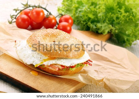 Sandwich bagel with fried bacon and egg on chopping board