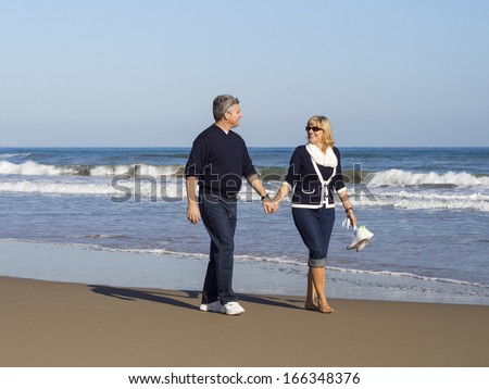 Attractive romantic mature couple walking along the beach hand in hand at the edge of the sea enjoying the beauty of the seaside and tranquillity of nature