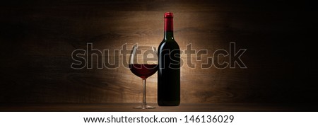 green bottle with red wine and glass on a wood panorama background