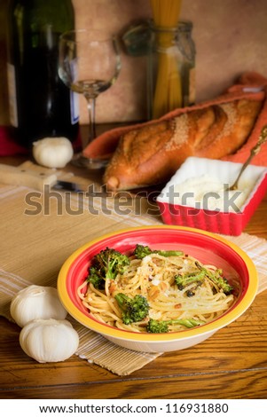 Traditional Italian meal of spaghetti with broccoli in setting with bread, garlic, cheese and wine