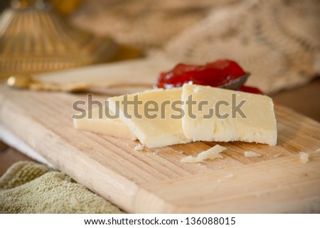 White cheddar cheese slices on cutting board with strawberry jam in the background