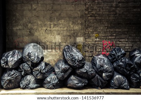 Black trash bags piled up against grungy urban wall