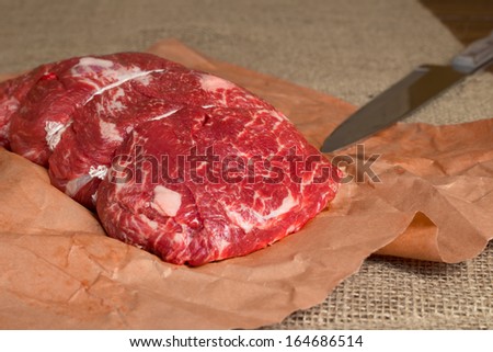 Lean cut of raw beef on butcher paper with knife