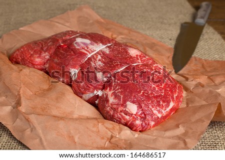Lean cut of raw beef on butcher paper with knife