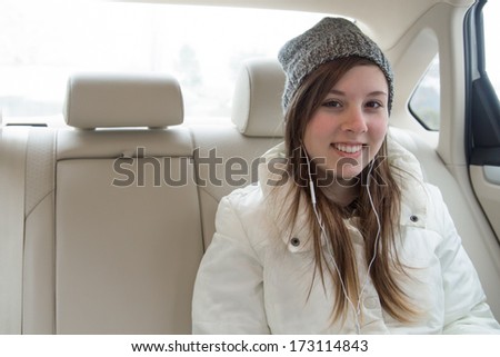 Cute teenage girl with hat and earbuds in backseat of car