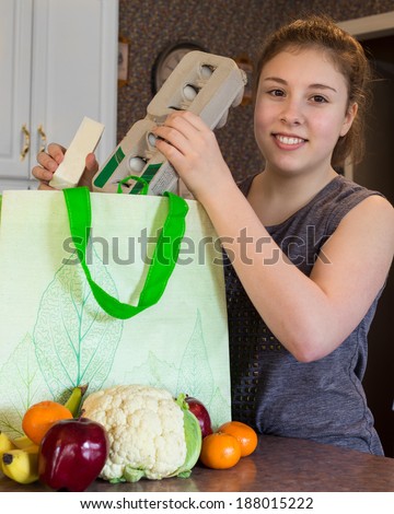 Cute girl unpacking healthy groceries from a reusable green bag