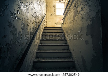 Dark grungy staircase with bright window in abandoned home