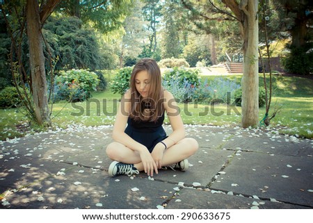 Pretty teenage girl sitting on ground in garden with soft filter effect