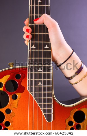 A girl\'s hand as she hold an acoustic guitar by the neck