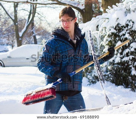 Young man removing snow after a storm with a broom