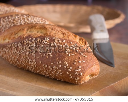 A loaf of seeded Italian bread with a knife and basket behind