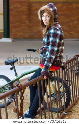 Cute teenage girl with a hood hanging out by the bike rack in the schoolyard