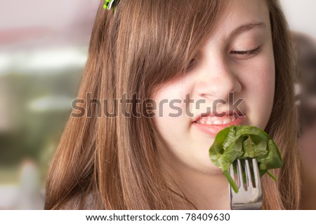 Cute girl making a disgusted face while eating greens