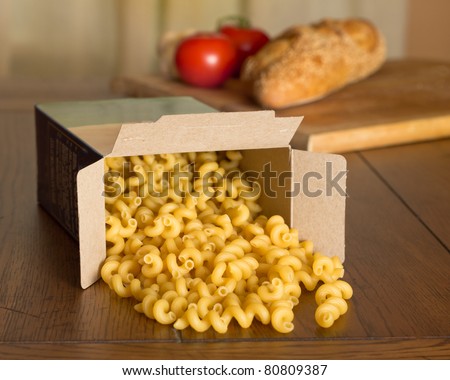 Italian cuisine cooking scene of cellentani type corkscrew pasta spilling out of the box with a loaf of Italian break and tomatoes in the background