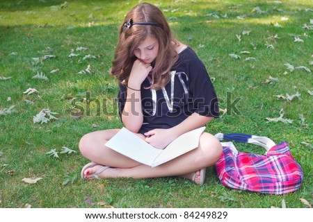 Cute teenage girl with book bag and notebook sitting in grass
