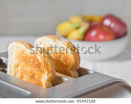Simple breakfast scene of toast in a toaster with a bowl of fruit behind