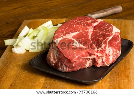 Raw beef chuck roast on a cutting board with chopped onion in preparation of a meal