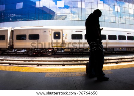 Silhouetted figure of a man with a cellphone standing on at a train station platform while train passes through