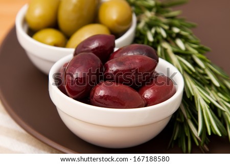 Bowls filled with pickled olives on clay plate. With lying side rosemary.