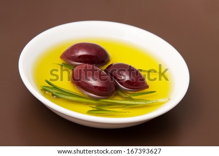 Bowl filled with olive oil and black pickled olives on brown clay plate.