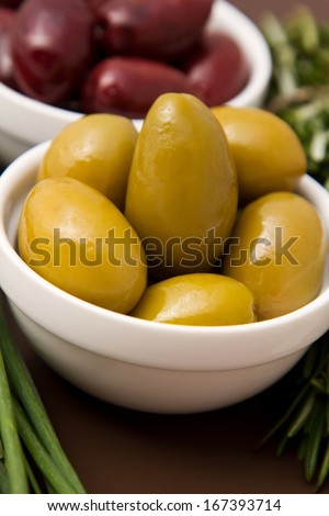 Bowls filled with pickled olives on clay plate. With lying side rosemary and chives.