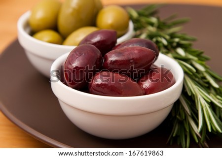 Bowls filled with pickled olives on clay plate. With a sprig of rosemary.
