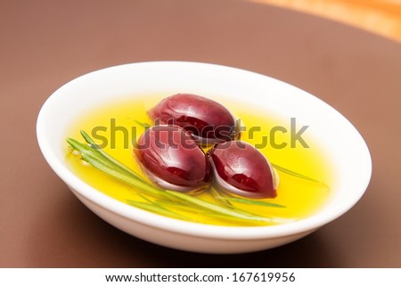 Bowl filled with olive oil and black pickled olives on clay plate.