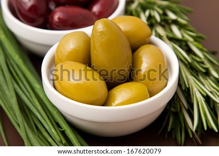 Bowls filled with pickled olives on clay plate. With chives and rosemary.