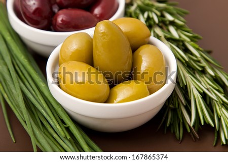 Bowls filled with pickled olives on clay plate. With a sprig of rosemary and chives.