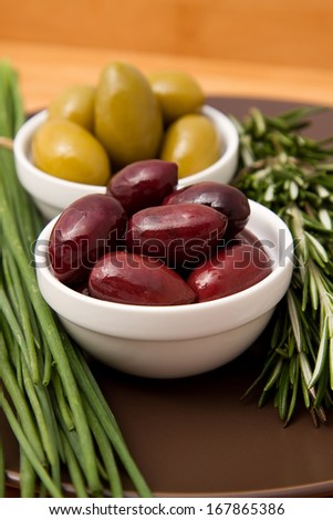 Bowls filled with pickled olives on clay plate. With a sprig of rosemary and chives.