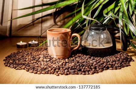 A cup of coffee with a jug of coffee on some coffee beans