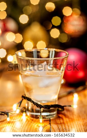 A glass of whiskey with christmas lights, ball and tree