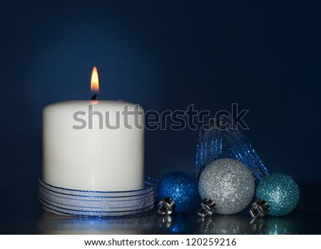 White Christmas candle burning, with glittering baubles on dark blue background