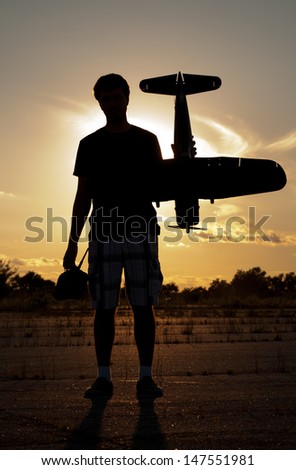 Silhouette of a young man with a model rc airplane against sunset sky