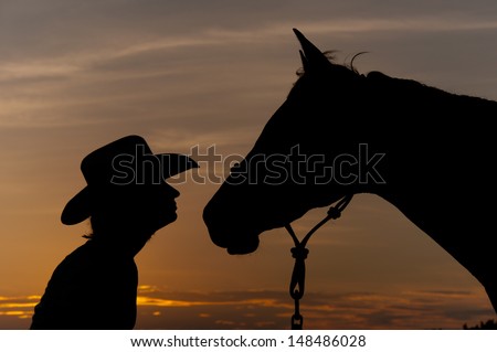 Silhouette of a girl in a cowboy hat with her horse, nose to nose - partners at sunset
