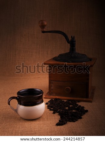 Cup of coffee with beans and an old grinder on the background, a warm toned image with vignette